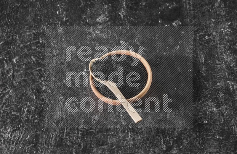 وعاء خشبي مع ملعقة خشبية ممتلئان ببذور حبة البركة علي خلفية سوداء