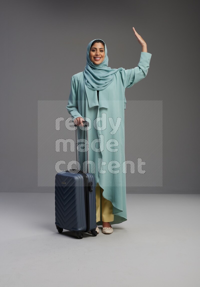Saudi Woman wearing Abaya standing holding Travel bag on Gray background