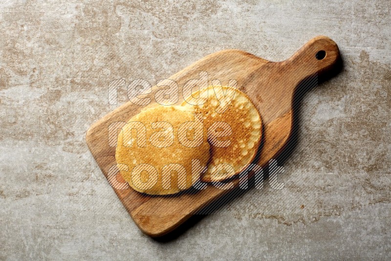 Two stacked plain pancakes on a wooden board on beige background