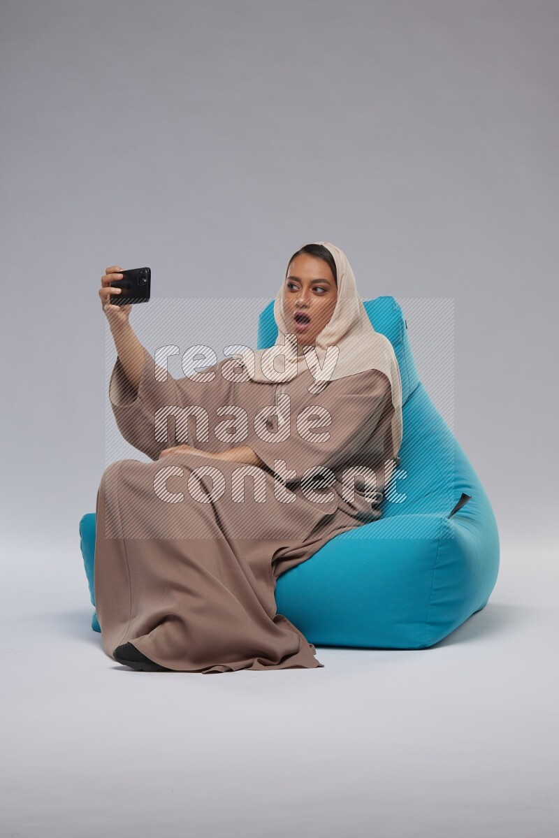 A Saudi woman sitting on a blue beanbag and taking selfie