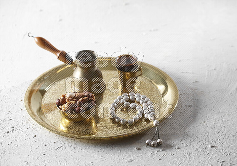 Nuts in a metal bowl with coffee and prayer beads on a tray in a light setup