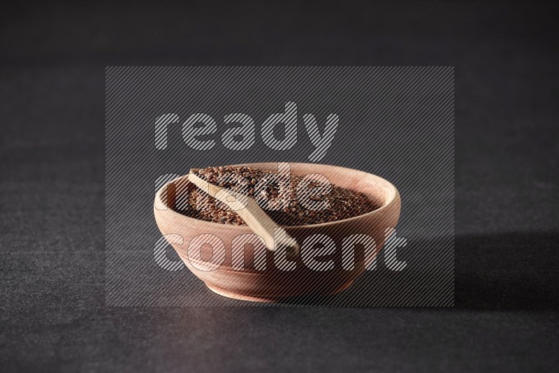 A wooden bowl full of flax with wooden spoon full of the seeds on it on a black flooring in different angles
