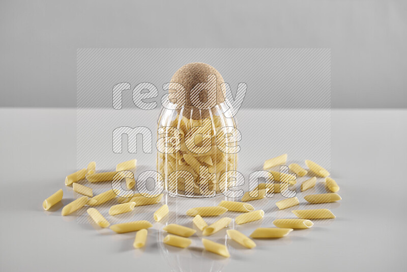 Raw pasta in a glass jar on light grey background