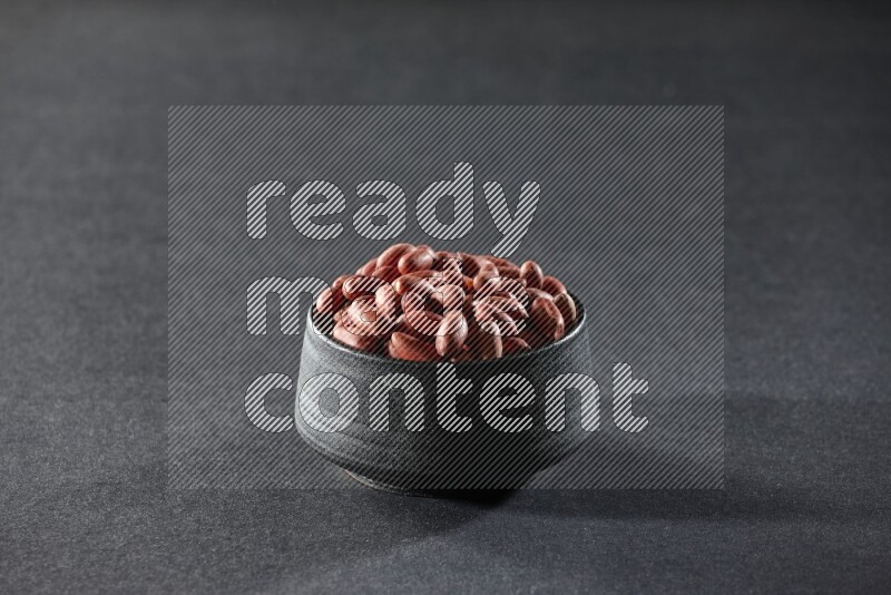 A black pottery bowl full of red skin peanuts on a black background in different angles