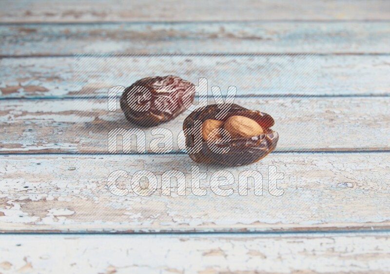 two almond stuffed madjoul dates on a light blue wooden background