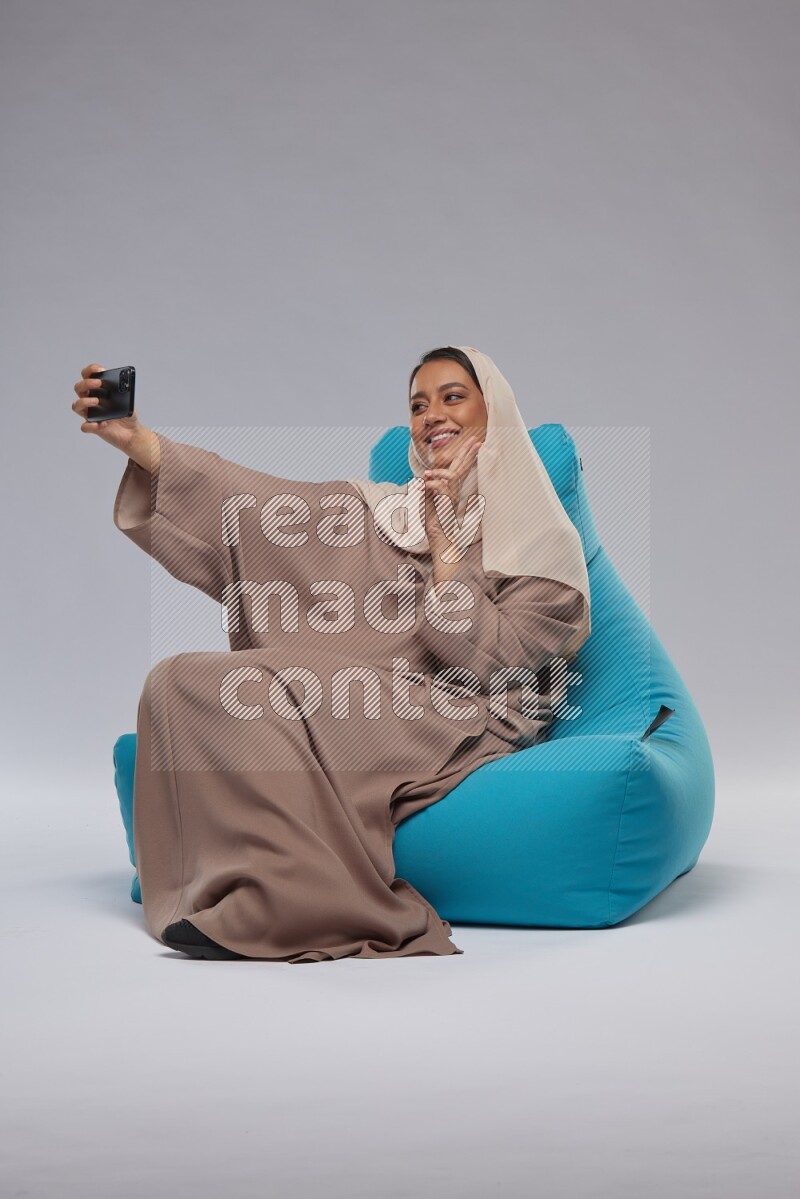 A Saudi woman sitting on a blue beanbag and taking selfie