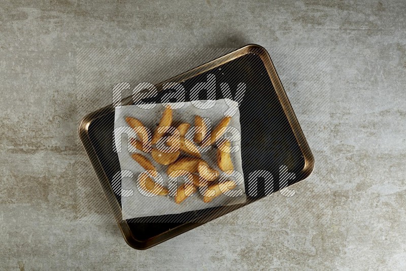wedges potato on parchment paper in a black stainless steel rectangle tray on grey textured counter top