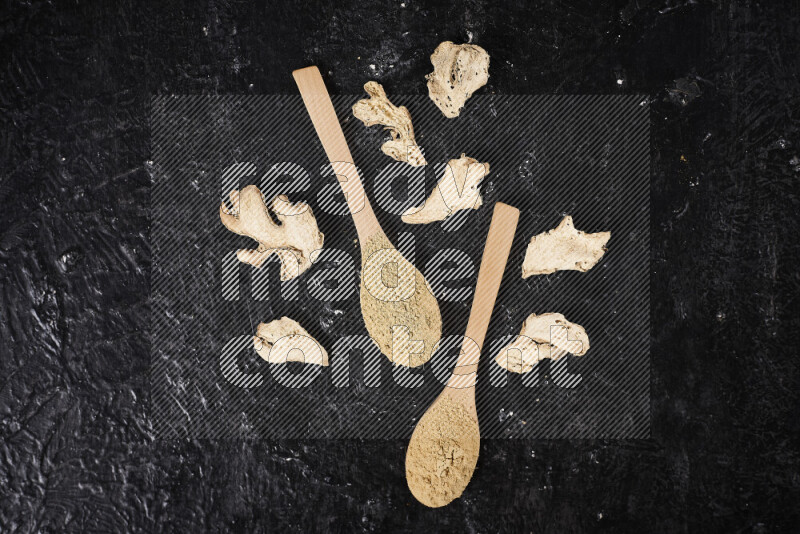 Two wooden spoons full of ground ginger powder on black background