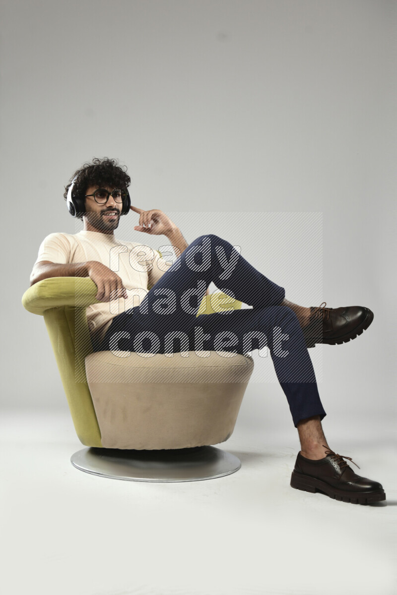 A man wearing casual sitting on a chair putting on headphones on white background
