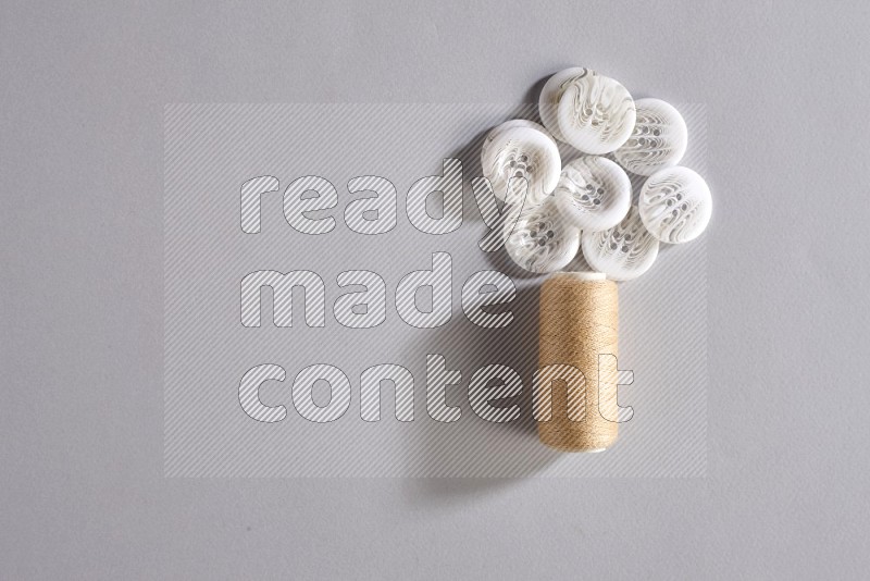 A beige sewing thread spool with colored buttons on grey background