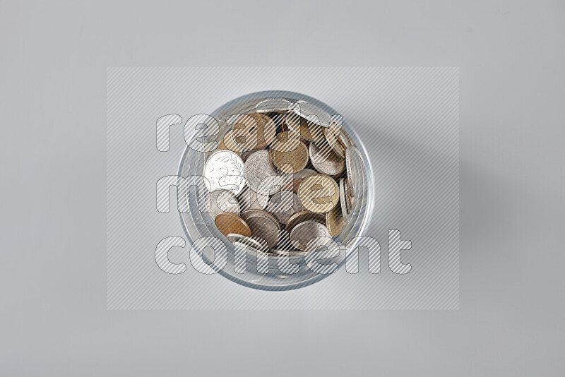 Random old coins in a glass cup on grey background