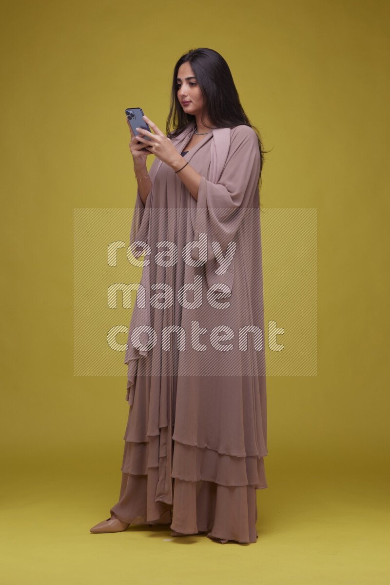 A woman Texting on a Yellow Background wearing Brown Abaya