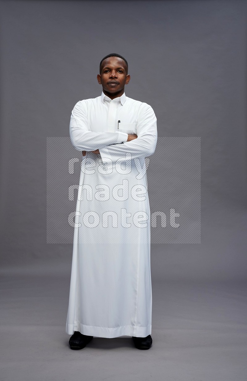 Saudi man wearing thob standing with crossed arms on gray background
