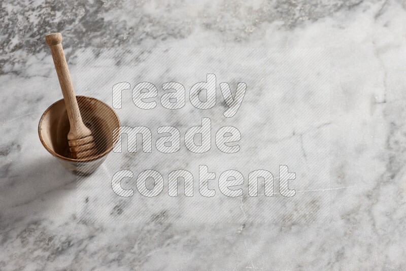 Decorative pottery bowl with wooden honey dipper in it on grey marble background