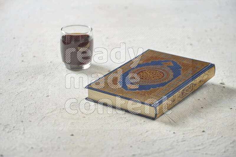 Quran with dates, prayer beads and different drinks all placed on textured white background