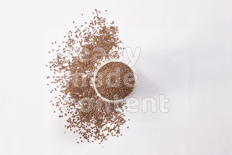 وعاء بيج فخاري ممتلئ بحبوب بذر الكتان مع بعض الحبوب المتناثرة علي خلفية بيضاء