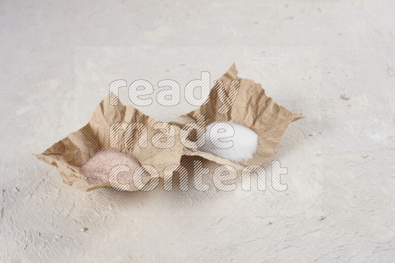 2 crumpled pieces of paper full of pink himalayan salt and white salt on white background