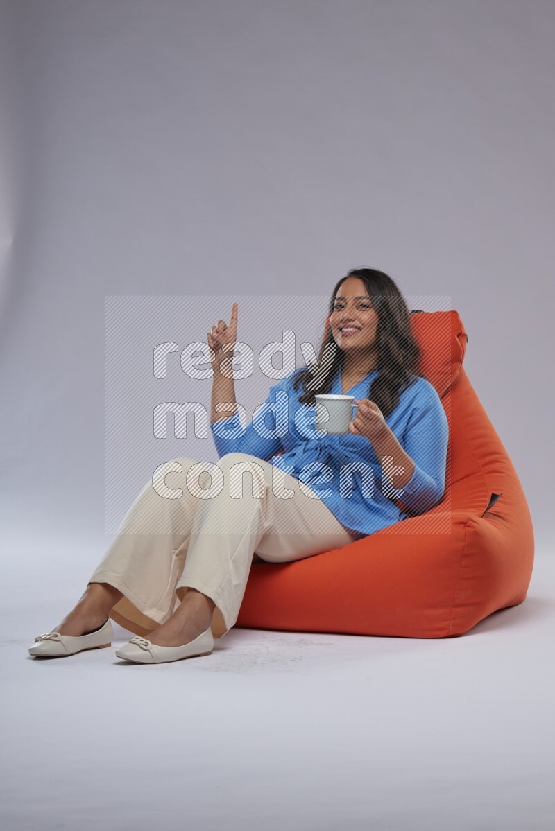 A woman sitting on an orange beanbag and drinking coffee
