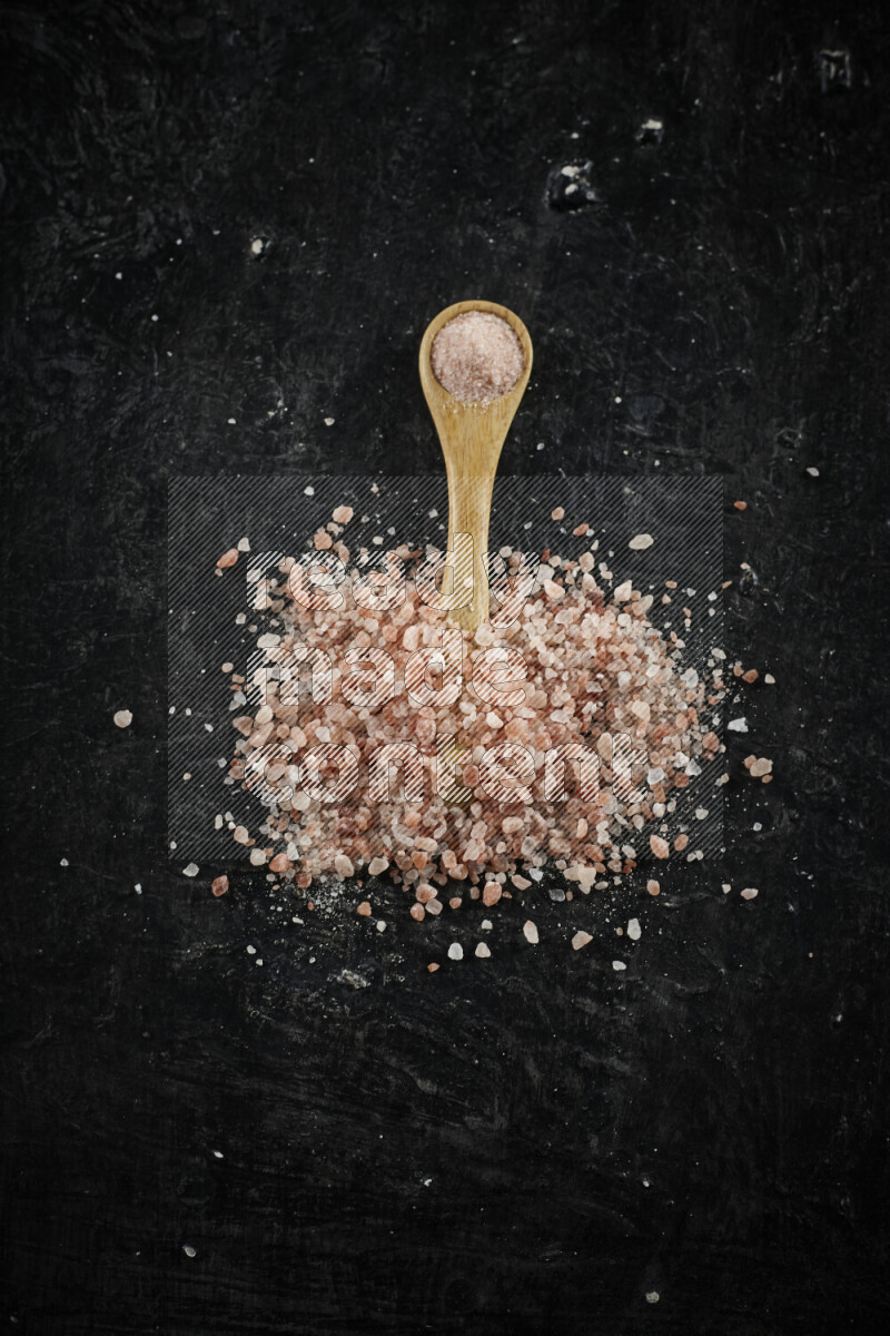 A wooden spoon full of pink himalayan salt on black background