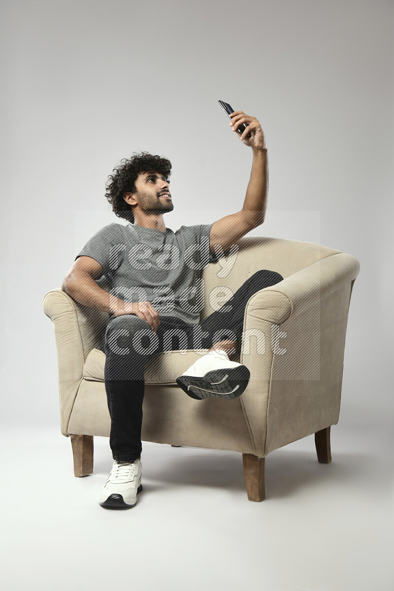 رجل يرتدي ملابس كاجوال يجلس علي كرسي و يلتقط صورة شخصية علي خلفية بيضاء