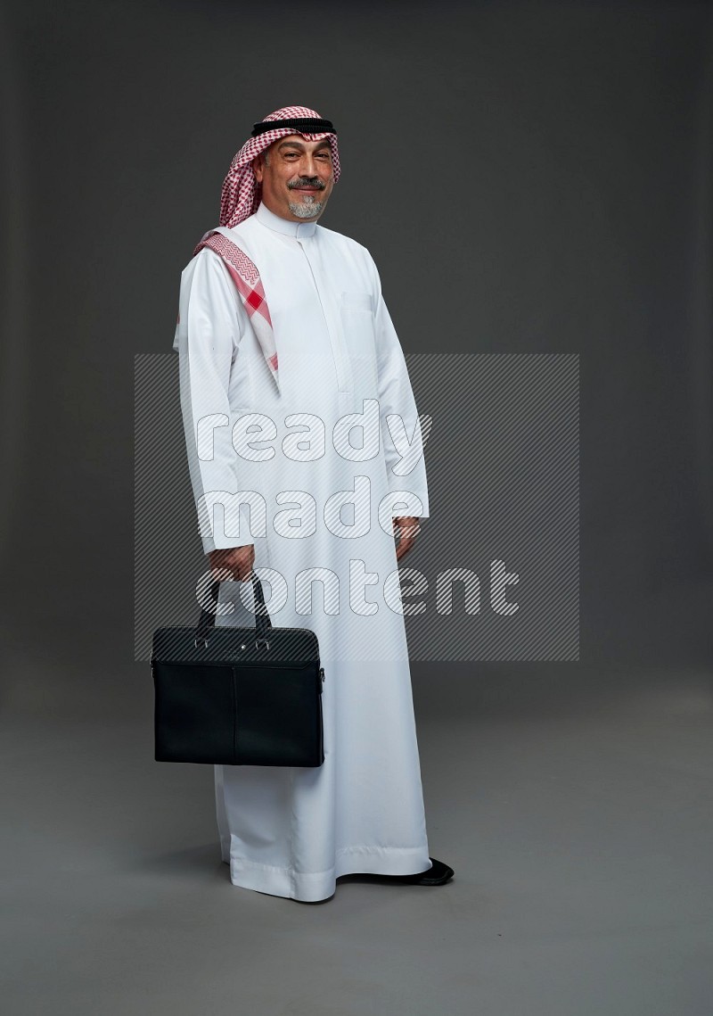 Saudi man with shomag Standing holding bag on gray background