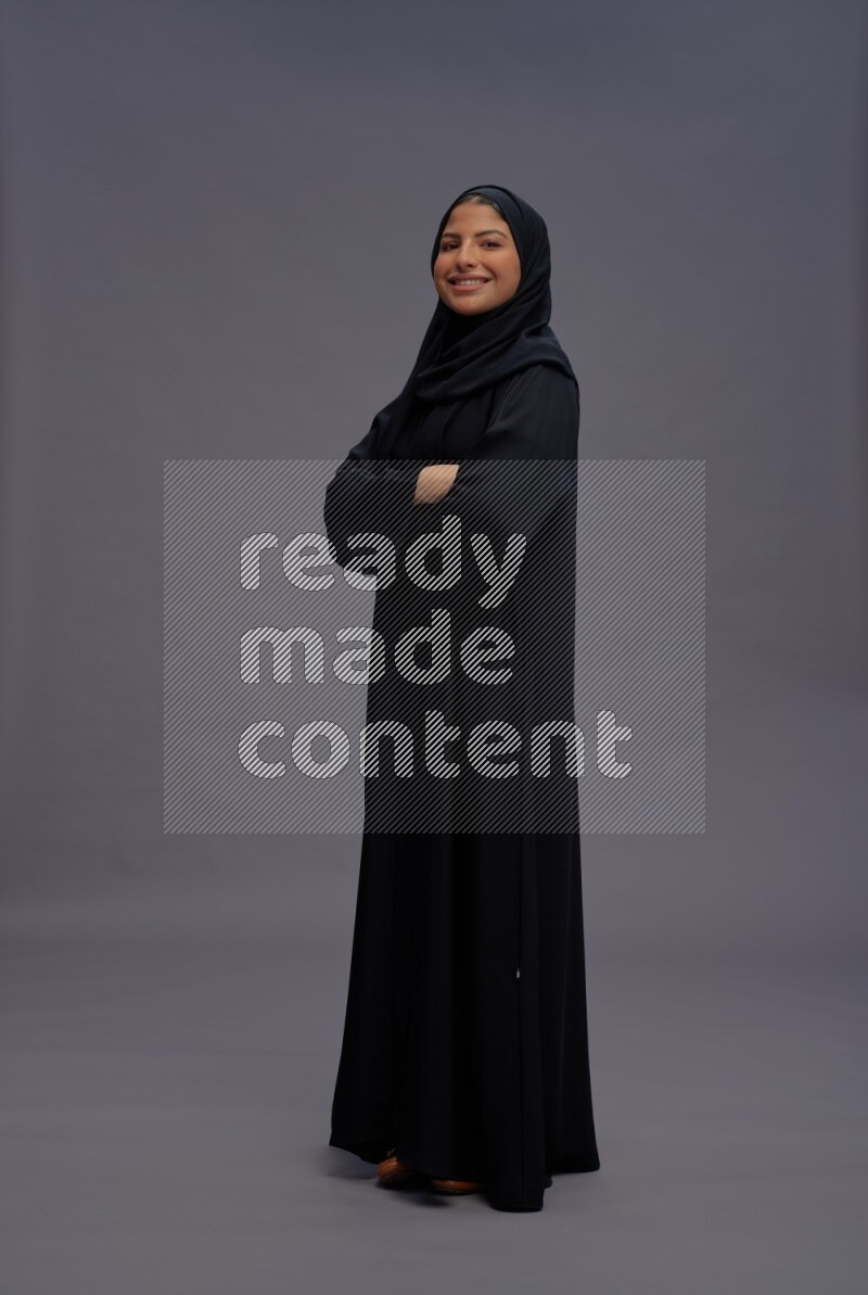 Saudi woman wearing Abaya standing with crossed arms on gray background