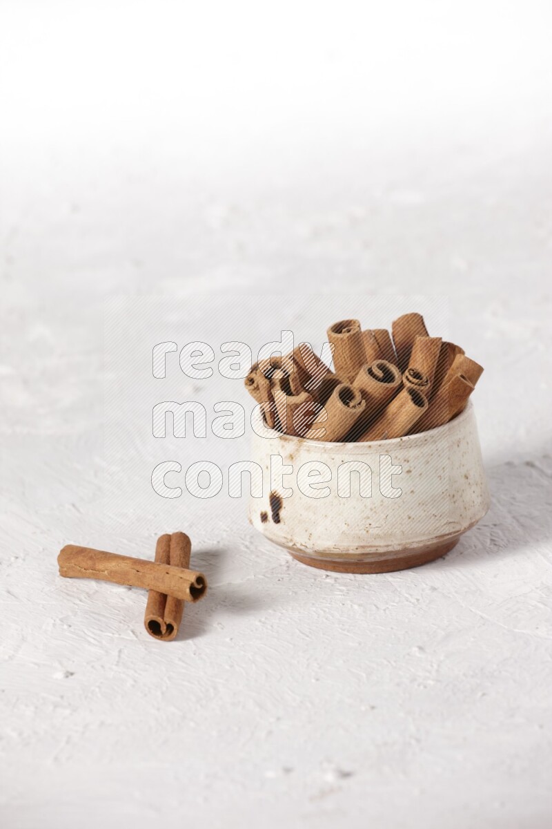 Cinnamon sticks in a beige bowl on a white background