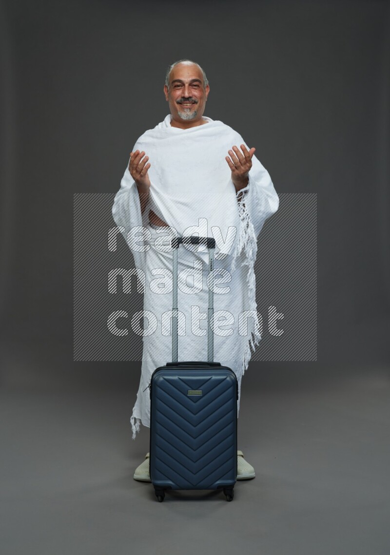 A man wearing Ehram Standing holding traveling bag on gray background