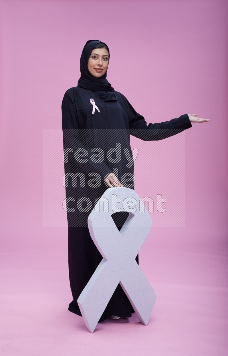 امرأة سعودية ترتدي عباية بشريطة زهرية وتقف وهي تحمل شريط التوعية على خلفية زهرية