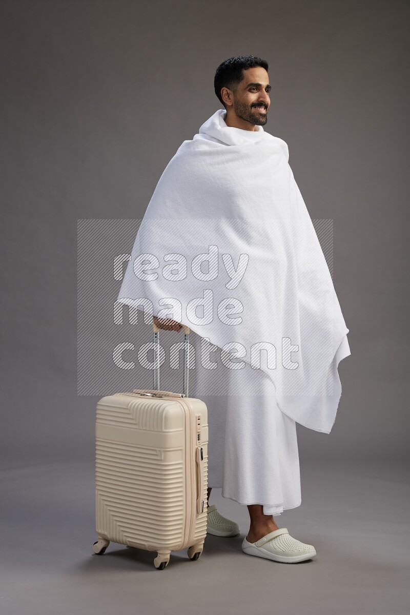 A man wearing Ehram Standing holding traveling bag on gray background
