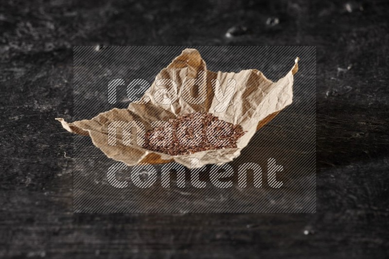 A crumpled piece of paper full of flaxseeds on a textured black flooring