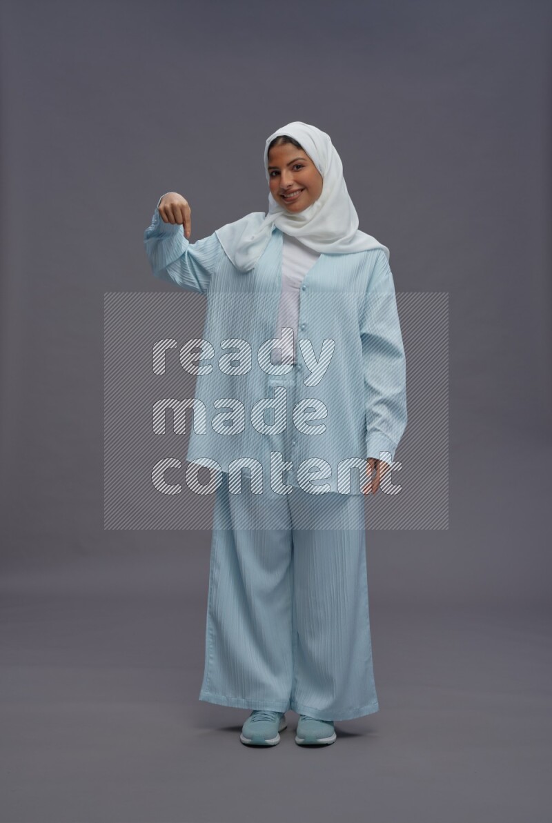 Saudi woman wearing hijab clothes standing interacting with the camera on gray background