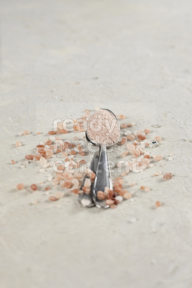 2 metal spoons filled with fine table salt and fine pink himalayan salt on white background