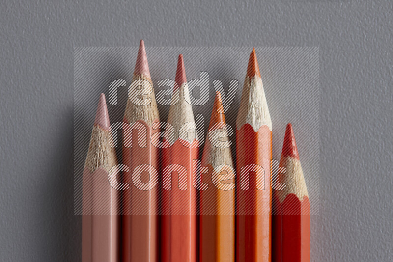 A collection of colored pencils arranged showcasing a gradient of orange hues on grey background