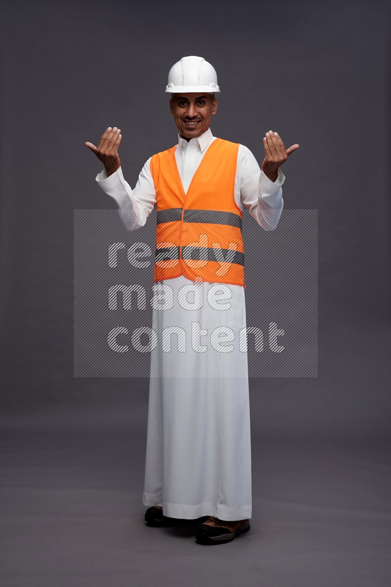 Saudi man wearing thob with engineer vest standing interacting with the camera on gray background