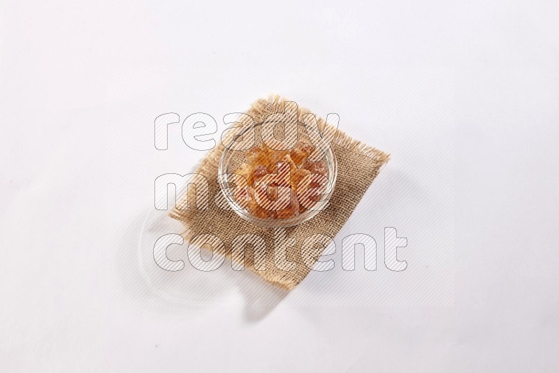 A glass bowl full of gum arabic on a burlap piece on white flooring