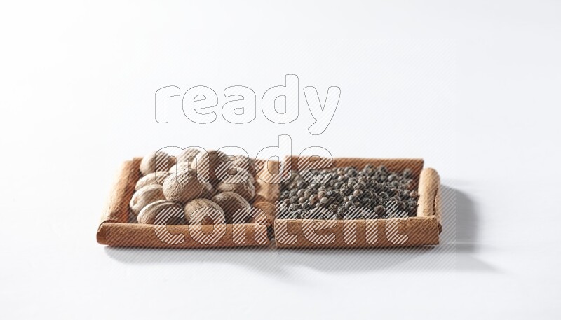 مربعان من أعواد القرفة ممتلئان بحبوب الفلفل الأسود وجوزة الطيب علي خلفية بيضاء