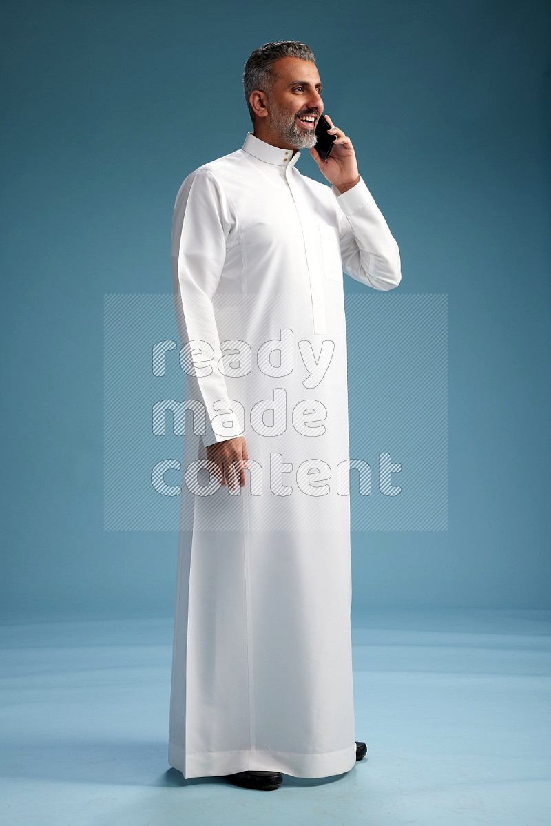 Saudi man wearing thob talking on the phone on blue background