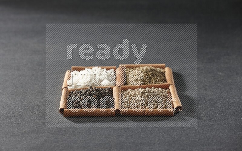 4 مربعات من عيدان القرفة ممتلئة بحبوب الفلفل الأسود والكمون وحبوب الفلفل الأبيض والملح الأبيض على أرضية سوداء