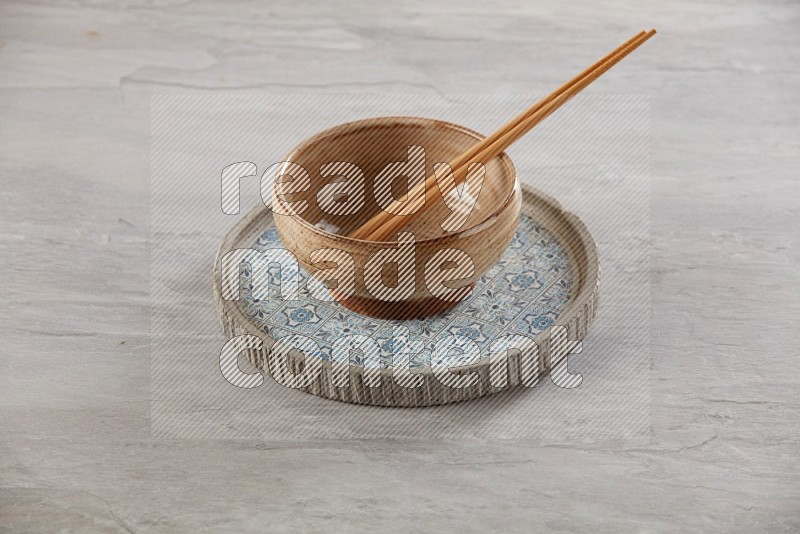 multi color pottery round bowl on top of multi color round ceramic plate and chopsticks, on grey textured countertop