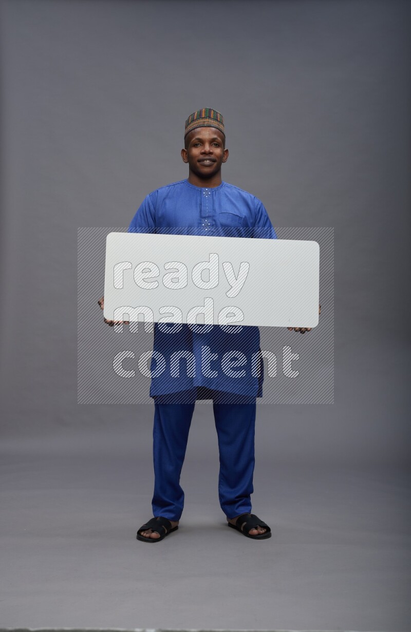 Man wearing Nigerian outfit standing holding board on gray background