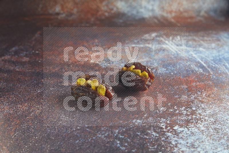 two pistachio stuffed madjoul dates on a rustic reddish background