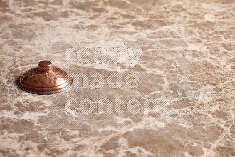 A small copper pot lid on beige marble background