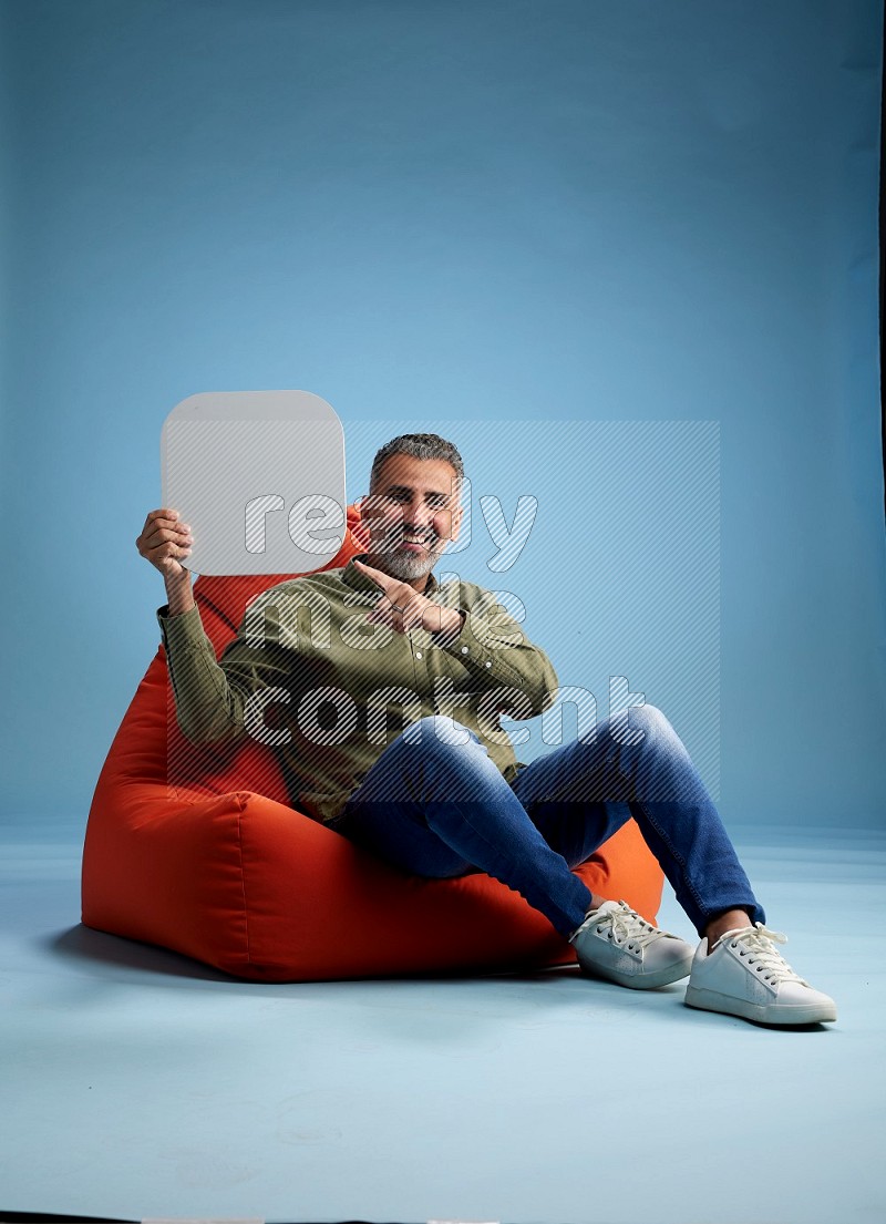 A man sitting on a orange beanbag and holding social media sign