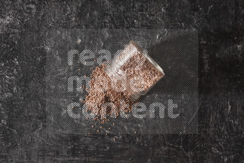 وعاء زجاجي مقلوب ممتلئ بحبوب بذر الكتان والحبوب متناثرة منه علي خلفية سوداء