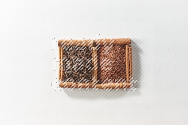 مربعان من أعواد القرفة ممتلئان بحب الرشاد والقرنفل علي خلفية بيضاء