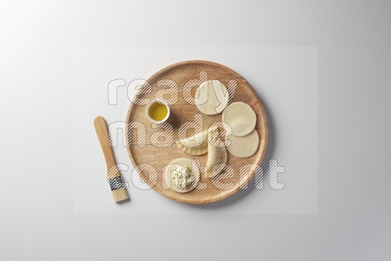 two closed sambosas and one open sambosa filled with cheese while oil with oil brush aside in a wooden dish on a white background