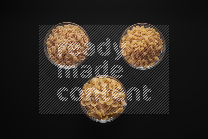 Different pasta types in glass bowls on black background