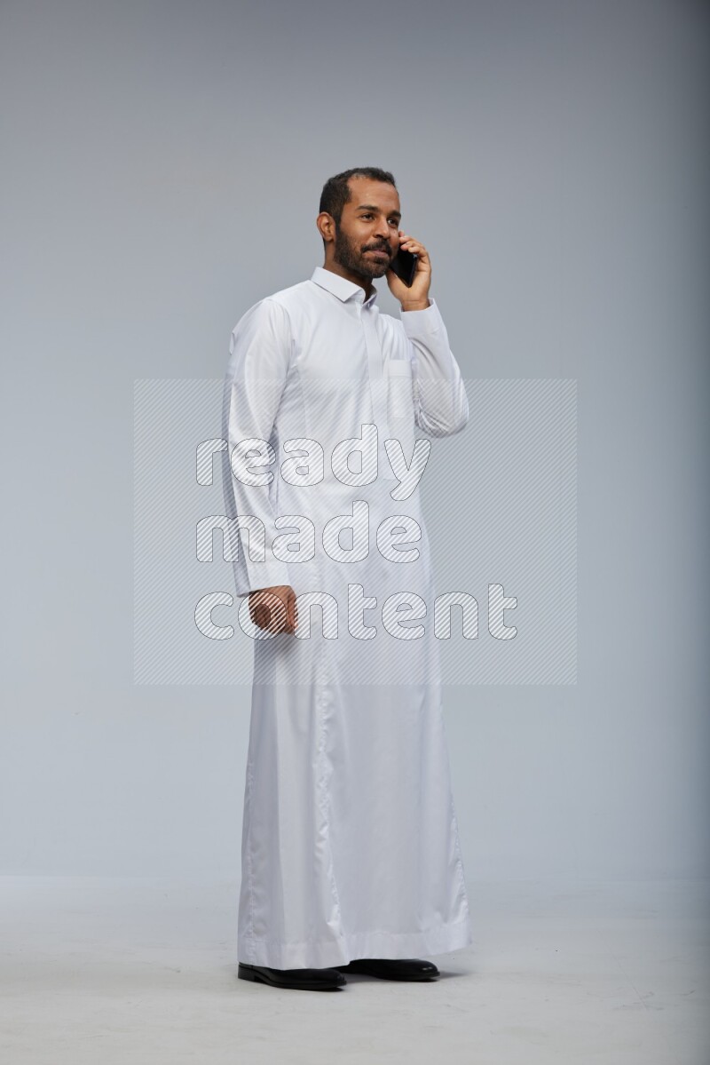 Saudi man wearing Thob standing talking on phone on Gray background
