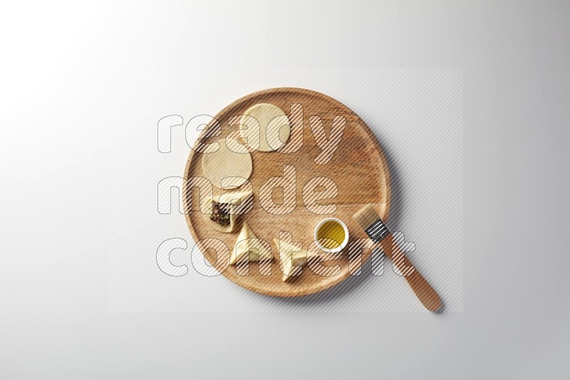 two closed sambosas and one open sambosa filled with meat while oil with oil brush aside in a wooden dish on a white background